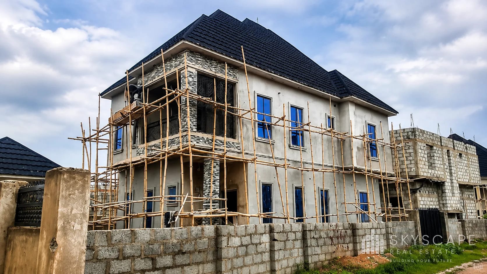Two-storey residential building at external finishing stage with decorative stone cladding and bamboo scaffolding